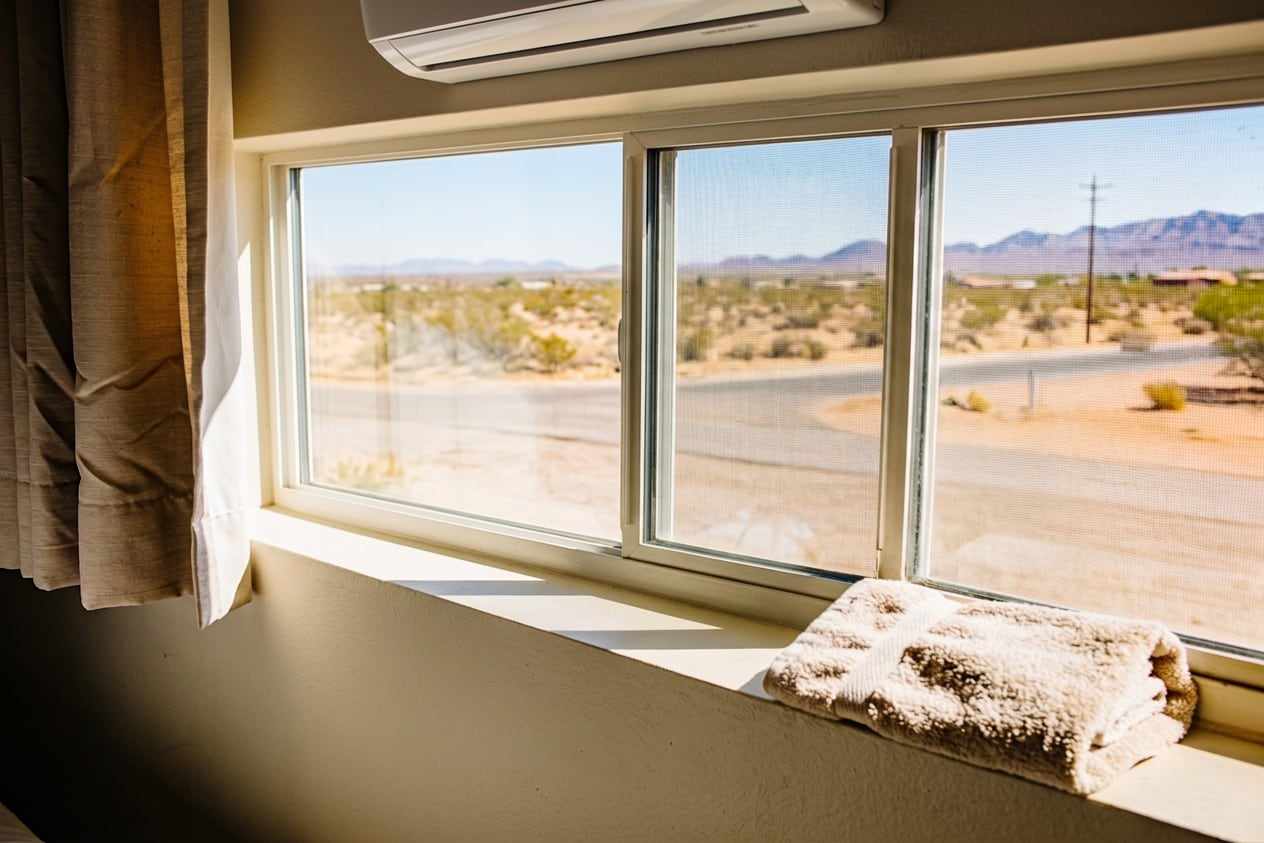 The same bedroom window clean and closed, a slim white mini-split on the wall above