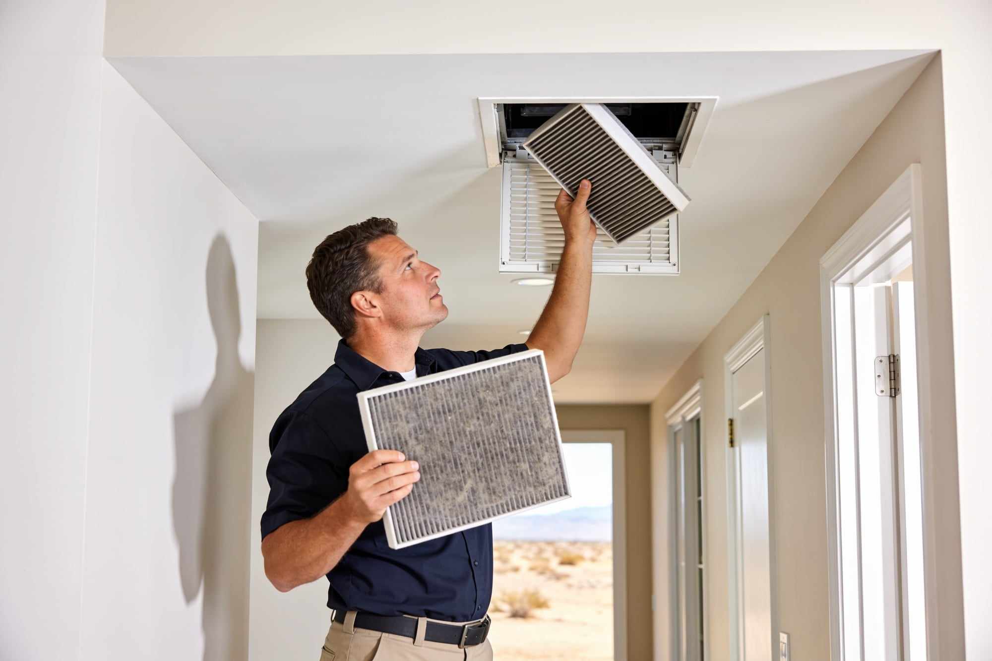 A technician fitting a fresh pleated filter into a ceiling return grille