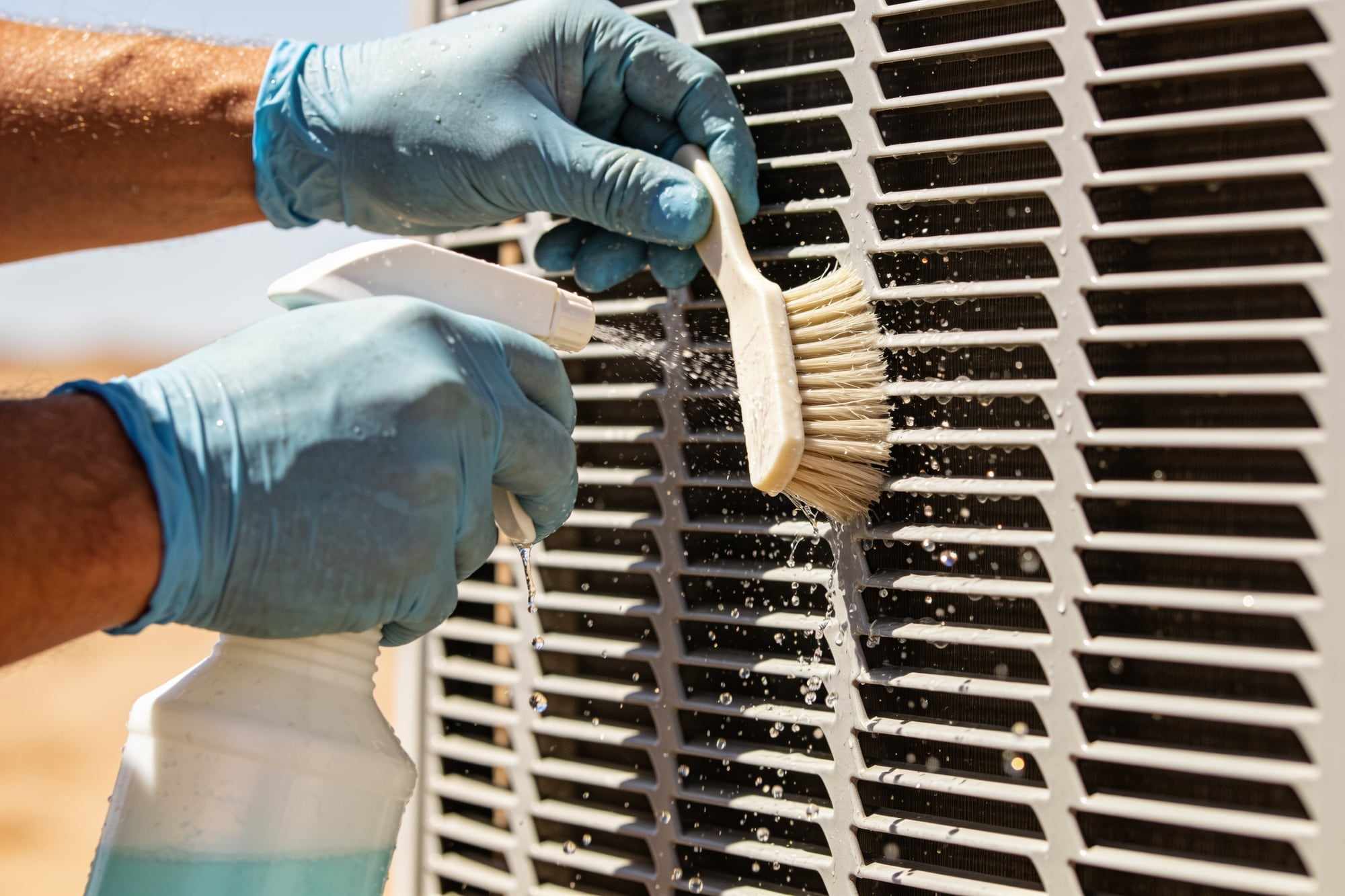 Gloved hands cleaning the fins of an outdoor AC coil with a soft brush